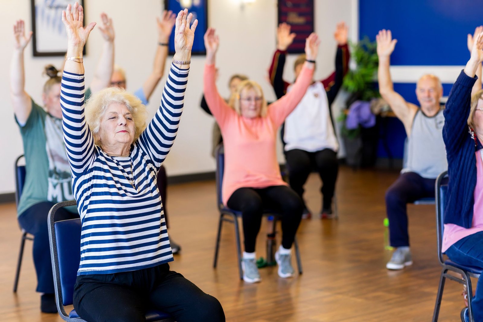 Chair yoga for seniors: older adults doing seated exercises on chairs with arms raised